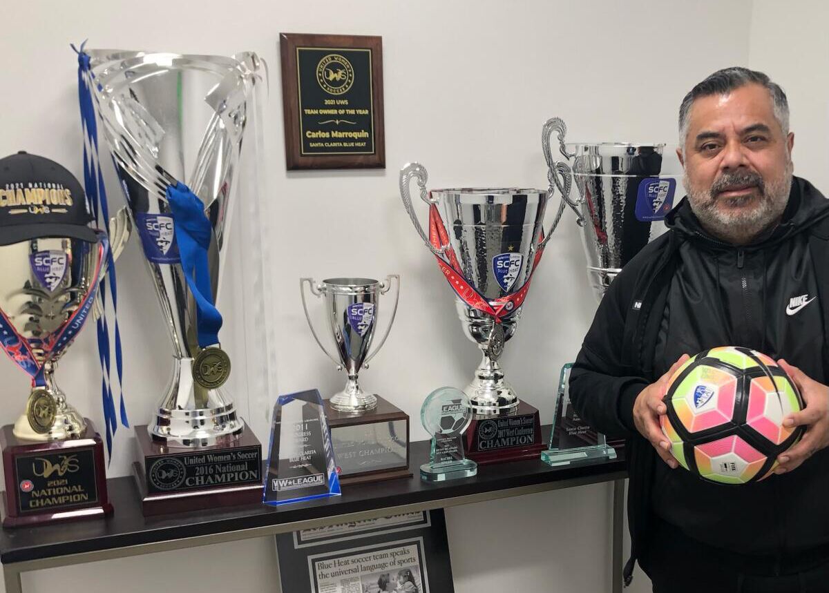 Carlos Marroquin stands next to trophies and awards won by the Santa Clarita Blue Heat.