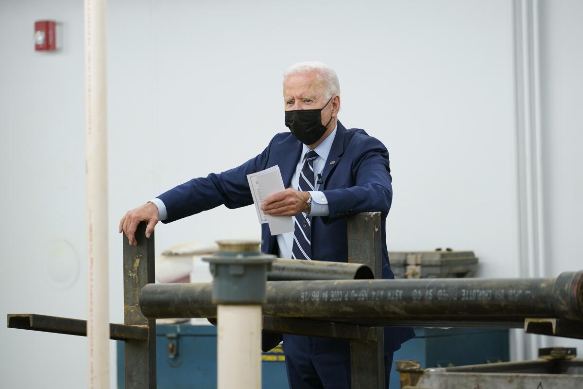 President Biden wears a mask and holds up pieces of paper.