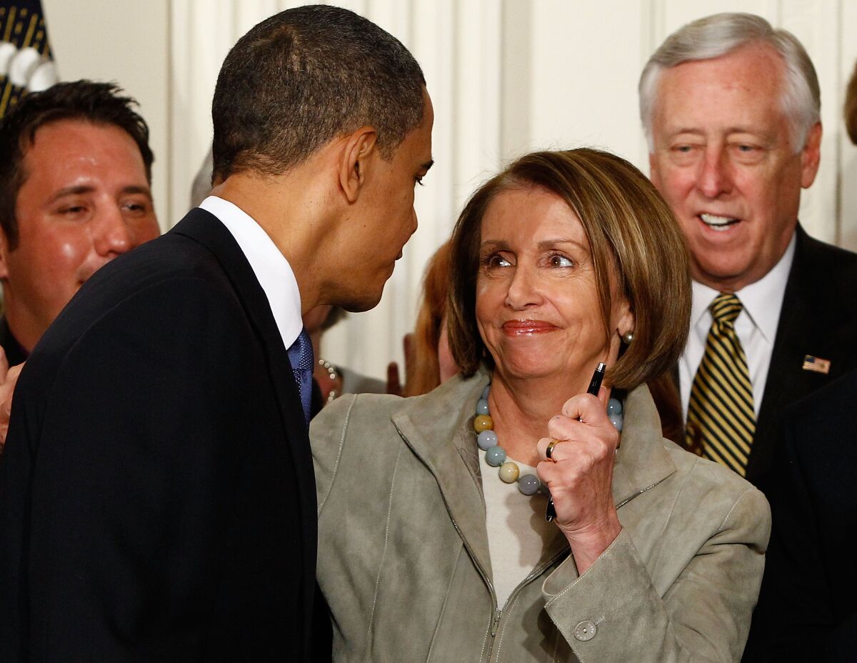 At that time, President Obama leans close to Speaker of the House Nancy Pelosi holding a pen while others look on