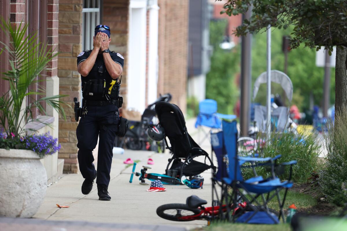 A police officer covers his eyes while walking among abandoned chairs, strollers and bikes in Highland Park, Ill.