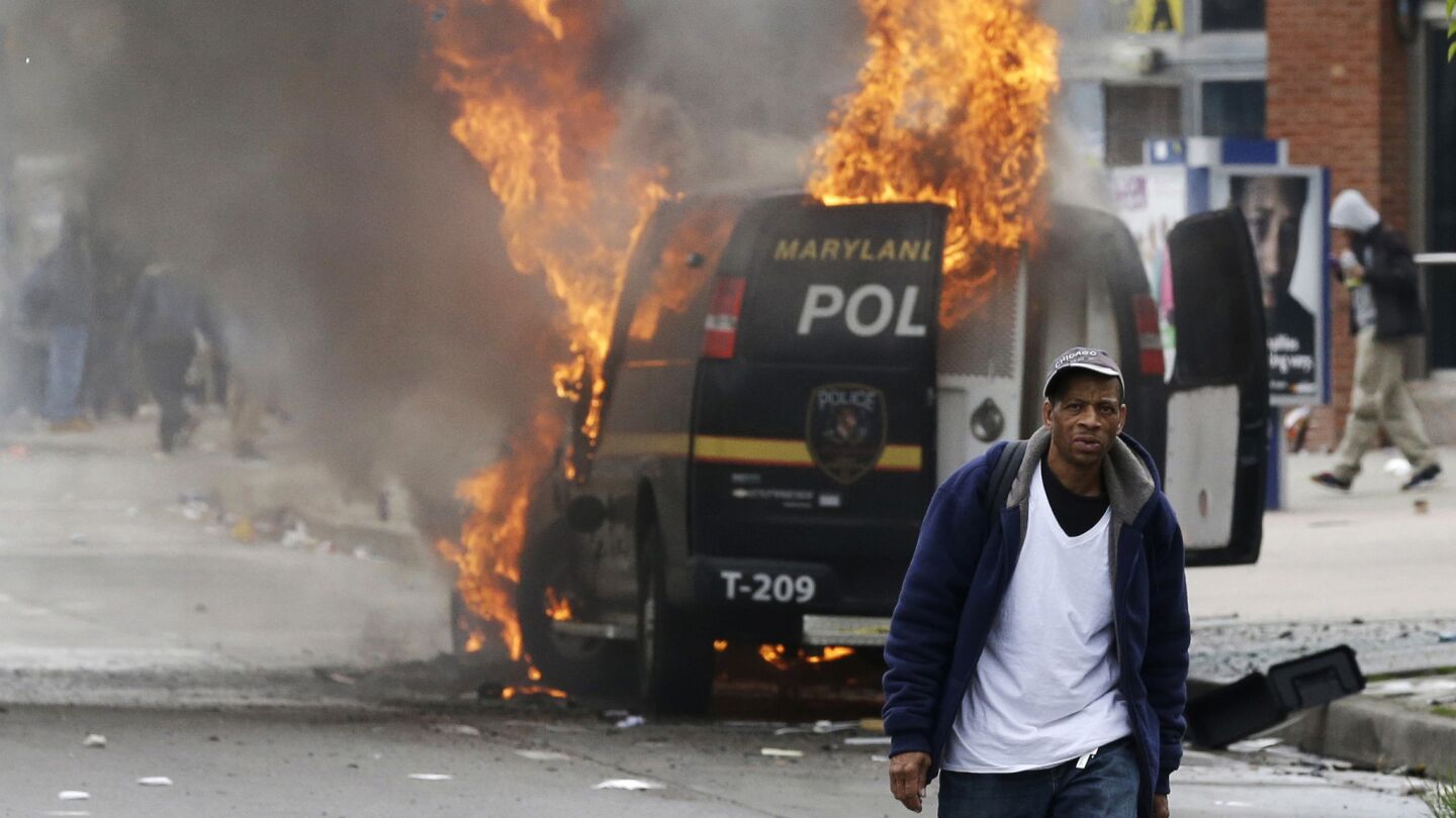 A man walks past a burning police vehicle during unrest after the funeral of Freddie Gray in Baltimore.