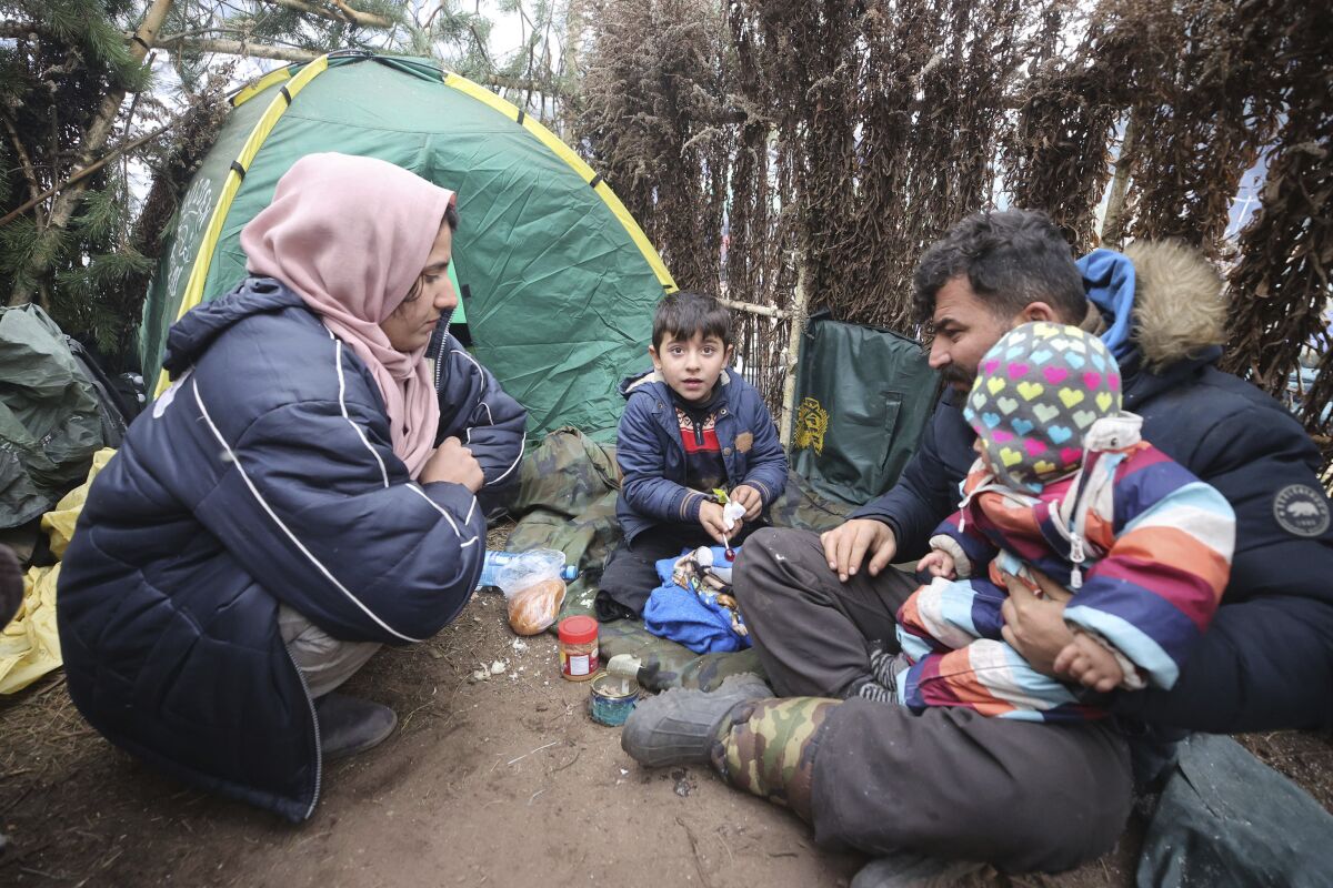 A family eat at a tent camp as migrants gather at the Belarus-Poland border near Grodno, Belarus, Saturday, Nov. 13, 2021. A large number of migrants are in a makeshift camp on the Belarusian side of the border in frigid conditions. Belarusian state news agency Belta reported that Lukashenko on Saturday ordered the military to set up tents at the border where food and other humanitarian aid can be gathered and distributed to the migrants. (Leonid Shcheglov/BelTA pool photo via AP)