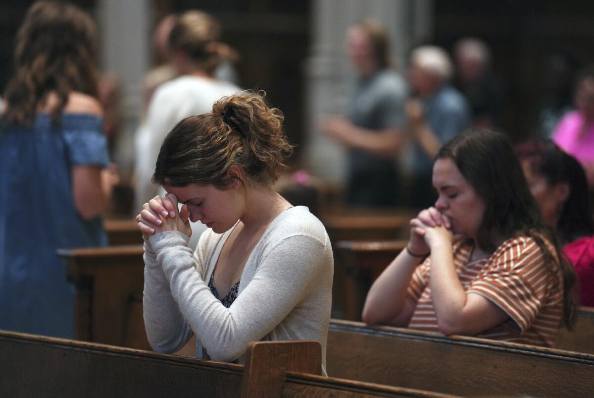 Two women kneel praying in pews.