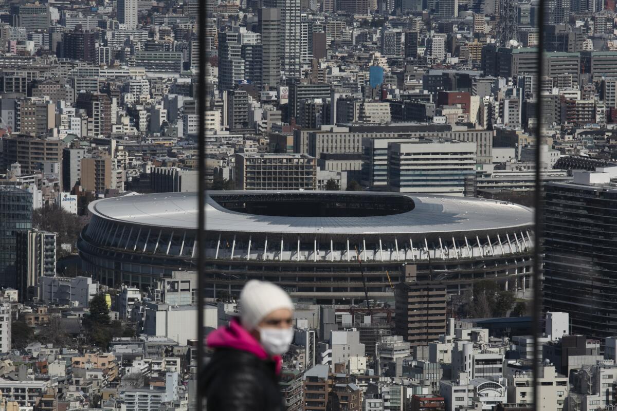 A man walks with a mask on with New National Stadium in the distance in Tokyo.