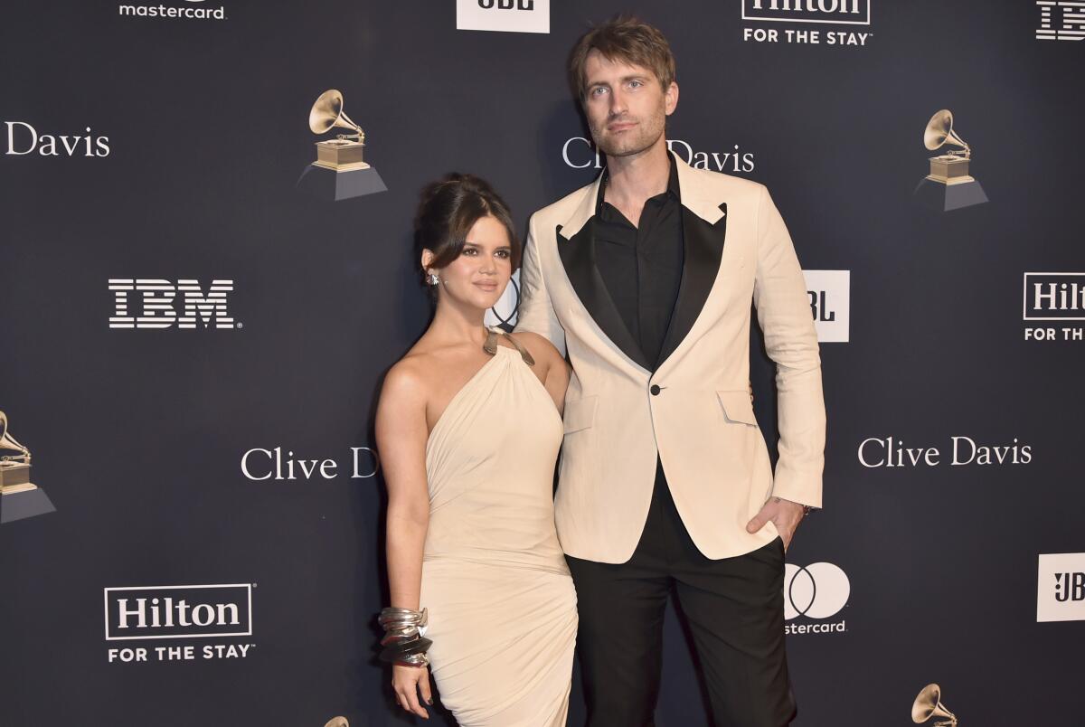 Maren Morris in a beige dress stands next to Ryan Hurd who wears a beige tuxedo jacket over black shirt and pants
