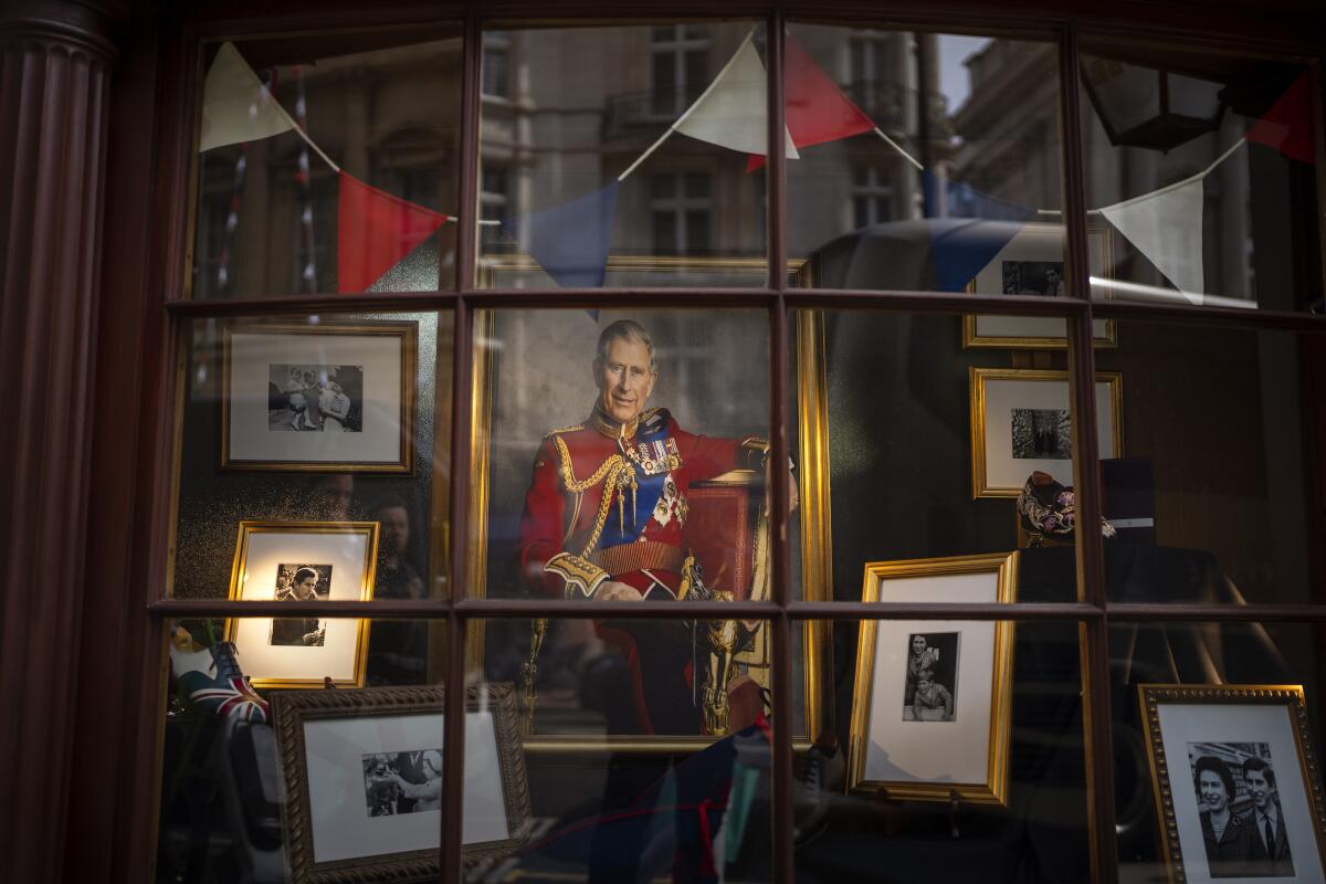 A storefront window decorated with framed photographs and a painting of King Charles III.