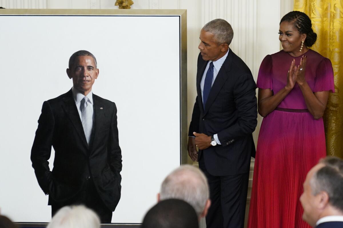 Michelle Obama applauds as the former president studies his own portrait.