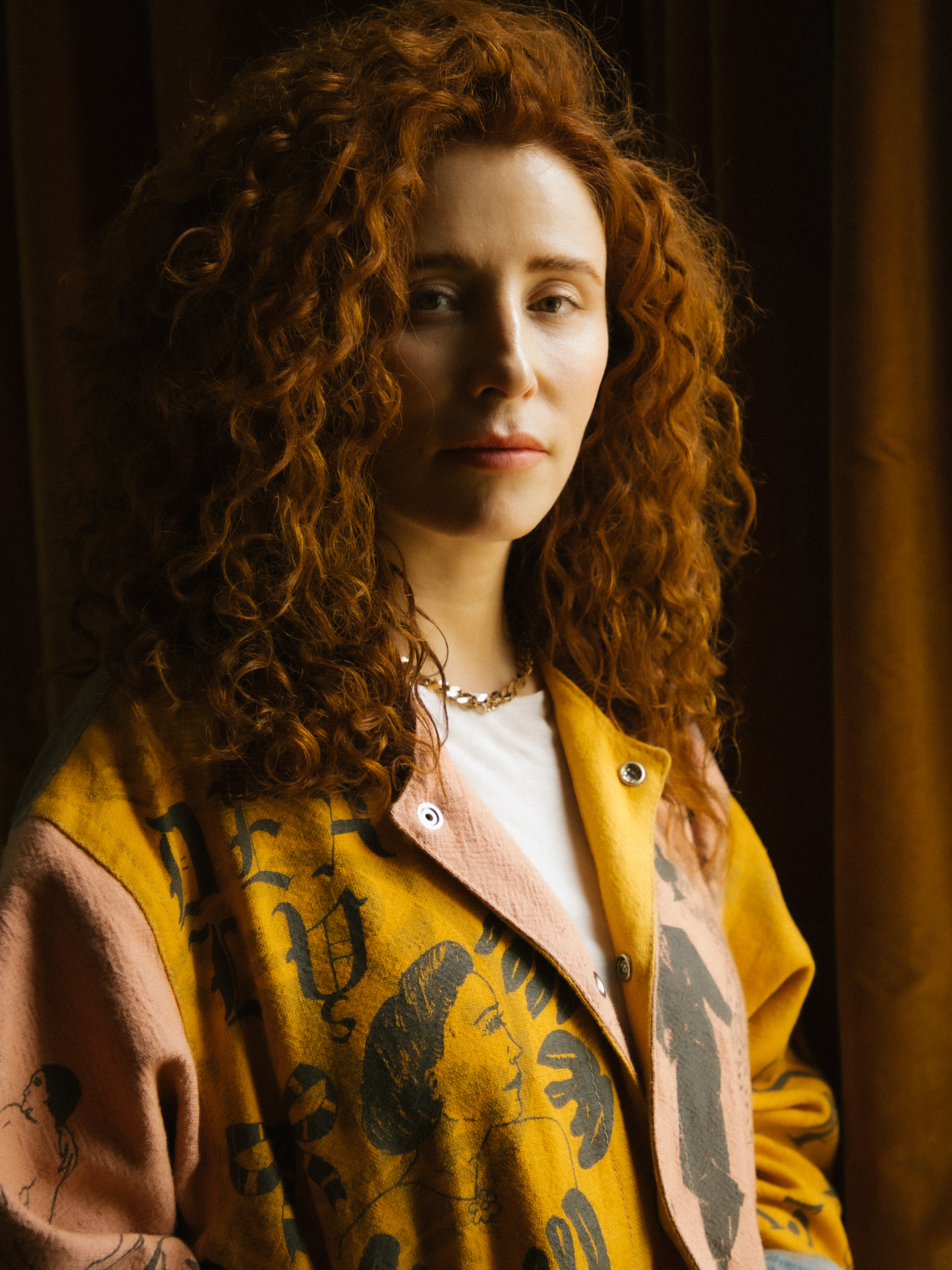 A woman with curly red hair in a yellow jacket.