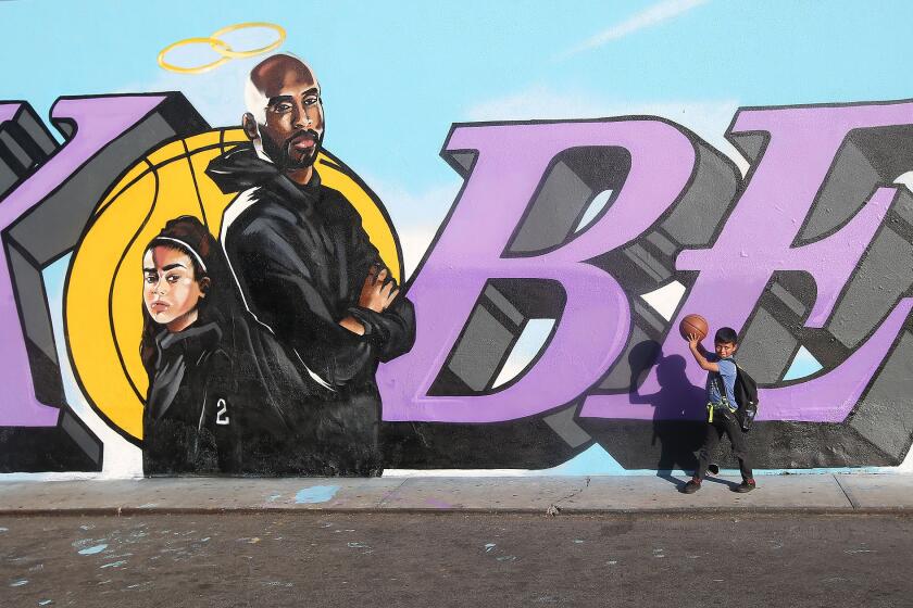 A youngster holds a basketball in front of a mural painted in honor of Kobe and Gianna Bryant over the last two days on the side of El Toro Bravo market in Costa Mesa. The artist is remaining relatively anonymous only know as @tykewitnesawr through his Instagram social media account.
