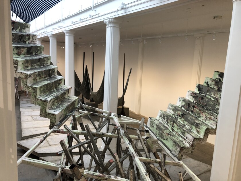 A set of sculptural stairs descend into a seemingly disorganized pile of wood in a room-sized art installation.