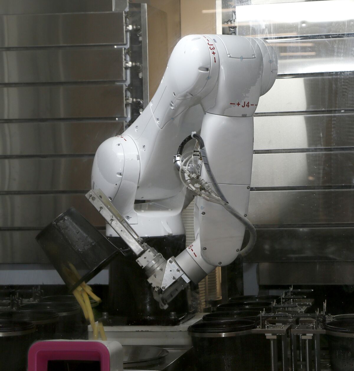 A robot arm drops french fries into a paper cup at the media dining hall in Beijing.