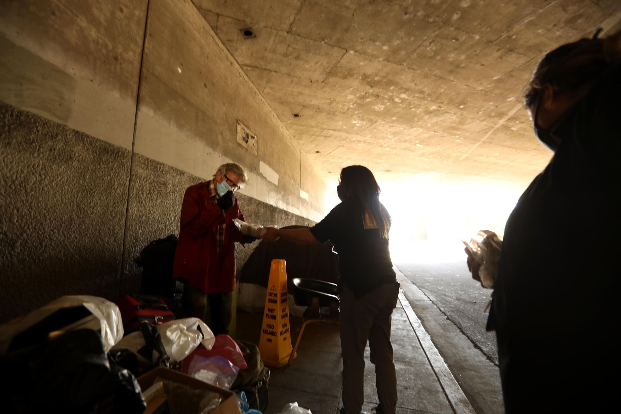 Outreach worker Judith Nuffio, center, gives Michael Cooper food while visiting his encampment under the 134 Freeway.