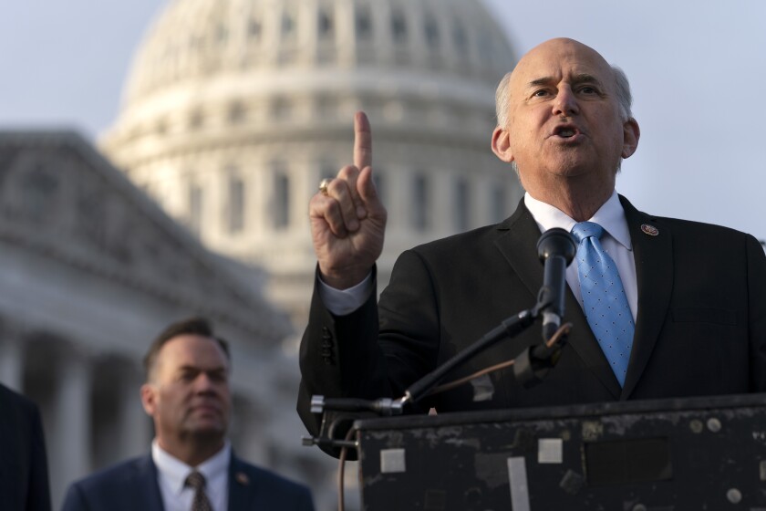 Rep. Louie Gohmert speaks at a lectern with the Capitol and a man in the background.