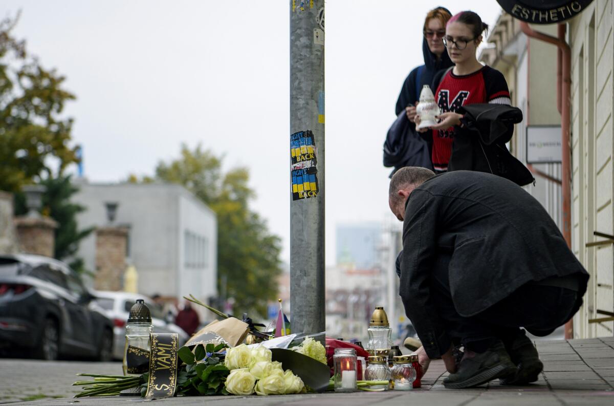 People lay flowers and light candles at the scene of Wednesday's attack on Zamocka Street in Bratislava, Slovakia, Thursday, Oct. 13, 2022. Slovakia’s police say they found the body of a suspect who allegedly fatally shot two people the previous day in the capital in what some officials are suggesting was a hate crime. Two men were killed and a woman was wounded on Wednesday evening near or at a bar which is a popular spot for the local LGBTQ community in downtown Bratislava. (Pavol Zachar/TASR via AP)