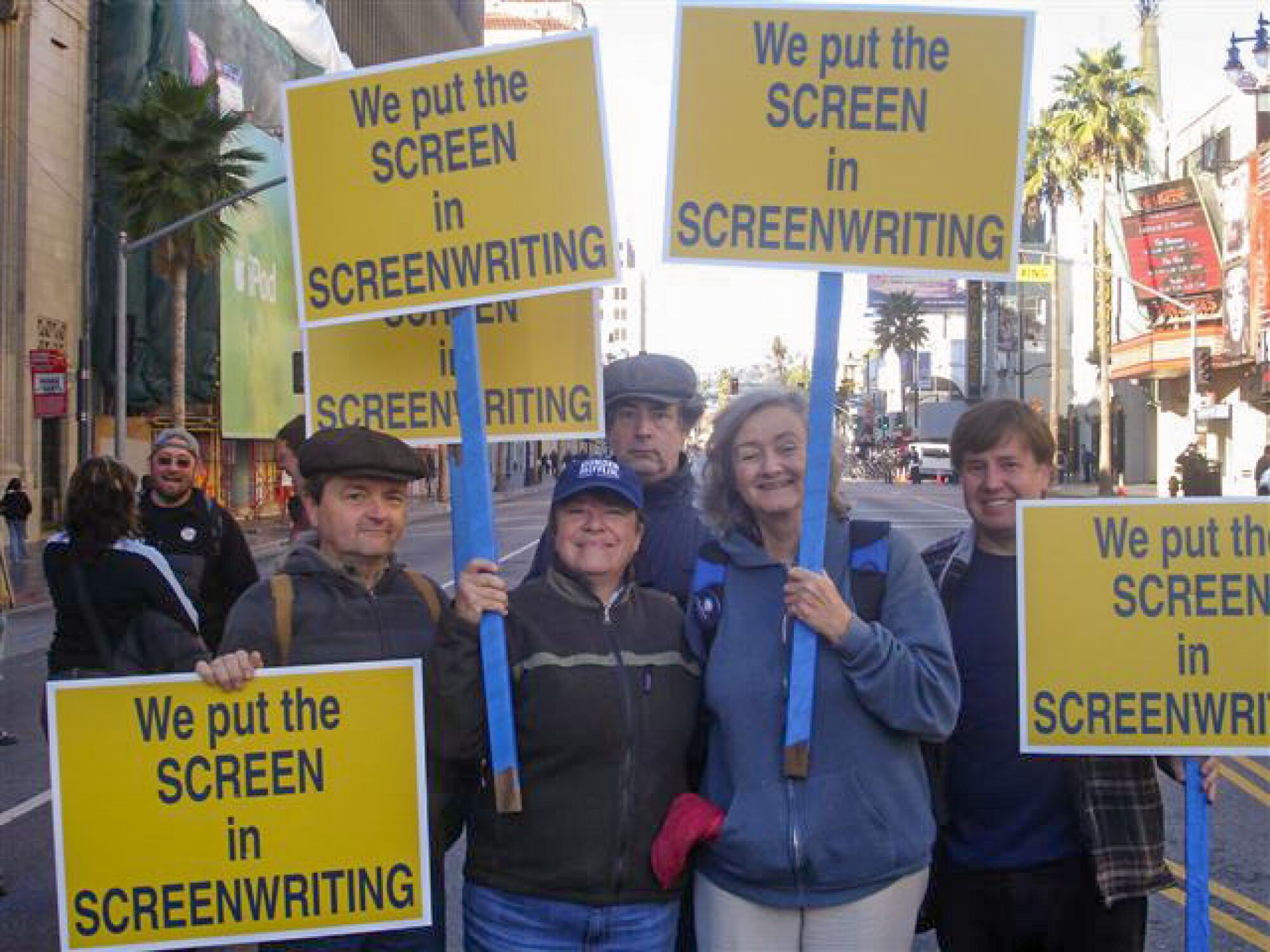 people hold yellow picket signs that say "we put the screen in screenwriting"