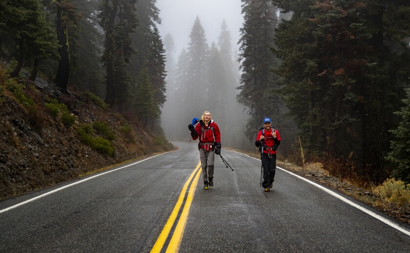Two men hike along a mountain highway in the mist.