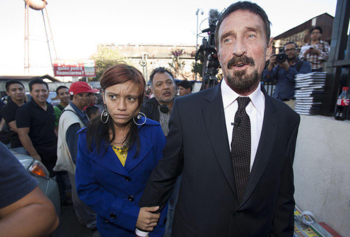 Software company founder John McAfee, right, accompanied by his girlfriend "Sam," exits a news conference outside the Supreme Court in Guatemala City on Tuesday. McAfee, 67, who has been identified as a "person of interest" in the killing of his neighbor in Belize, has surfaced in public for the first time in weeks, saying Tuesday that he plans to ask for asylum in Guatemala because he fears persecution in Belize, though it's unclear why he would need asylum because his travel has not been restricted.