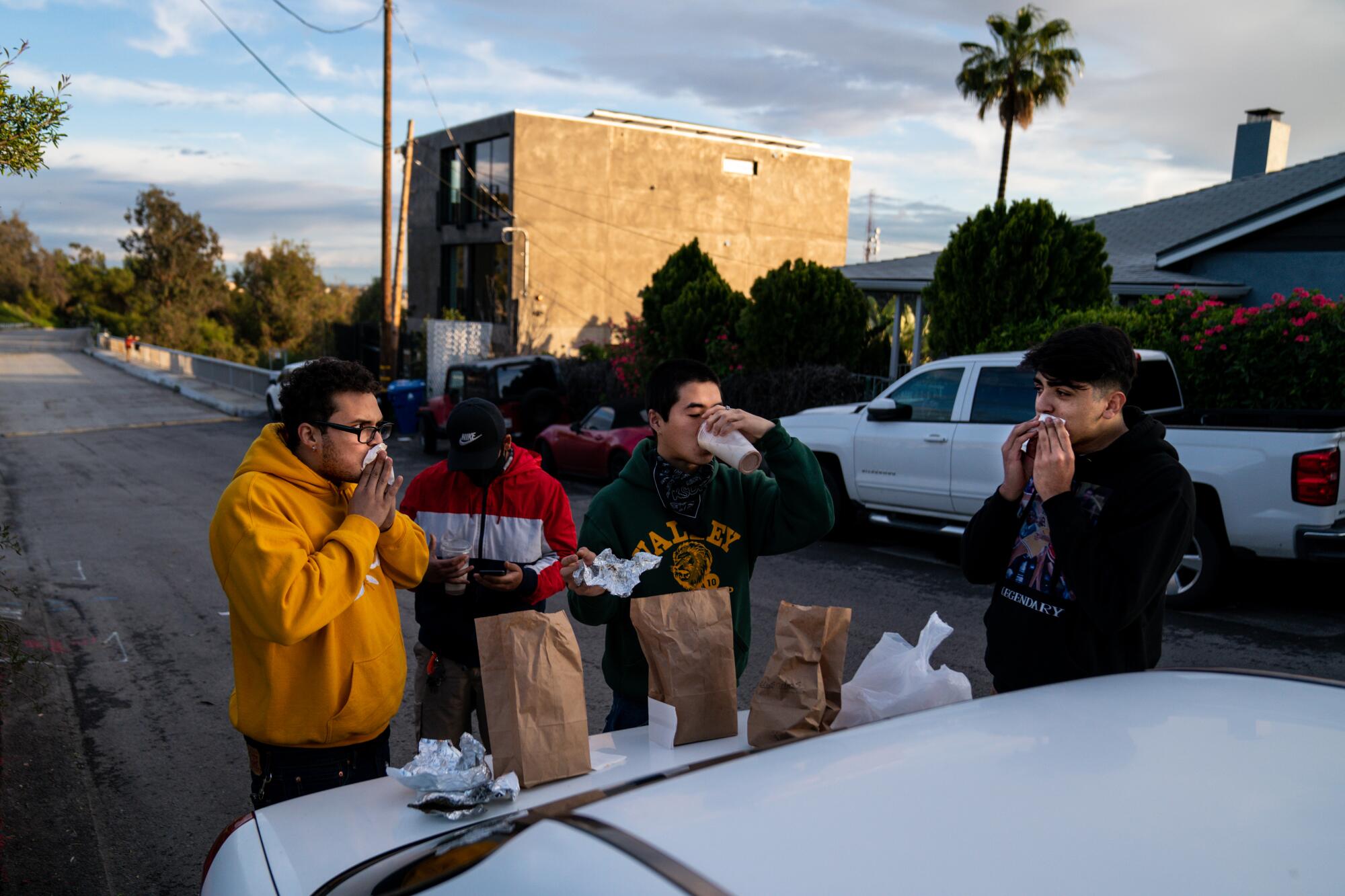 Anthony Calderon, 22, of Echo Park, David Escalante, 19, of Koreatown, Yun Park, 21, of Koreatown, and Antoine Montero, 19, of Los Feliz, eat food from Guisados on the trunk of a car in the Elysian Park neighborhood April 10 in Los Angeles.