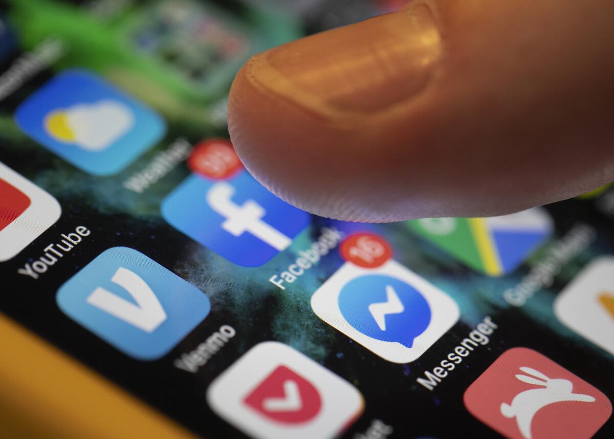  A finger is tapping an iPhone that displays social media apps.