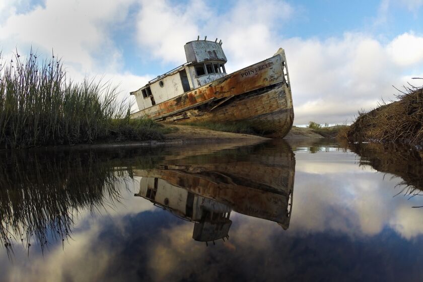A marooned fishing boat is reflected in low tide pools along Tomales Bay at Point Reyes National Seashore.