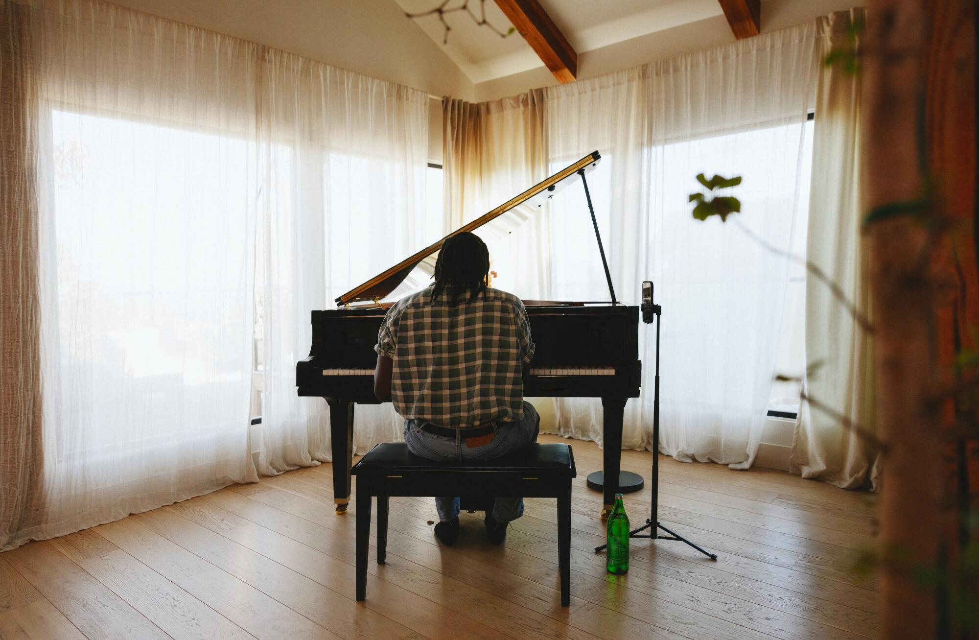 A man's back is seen while playing in the piano with gauze curtains at the bottom.