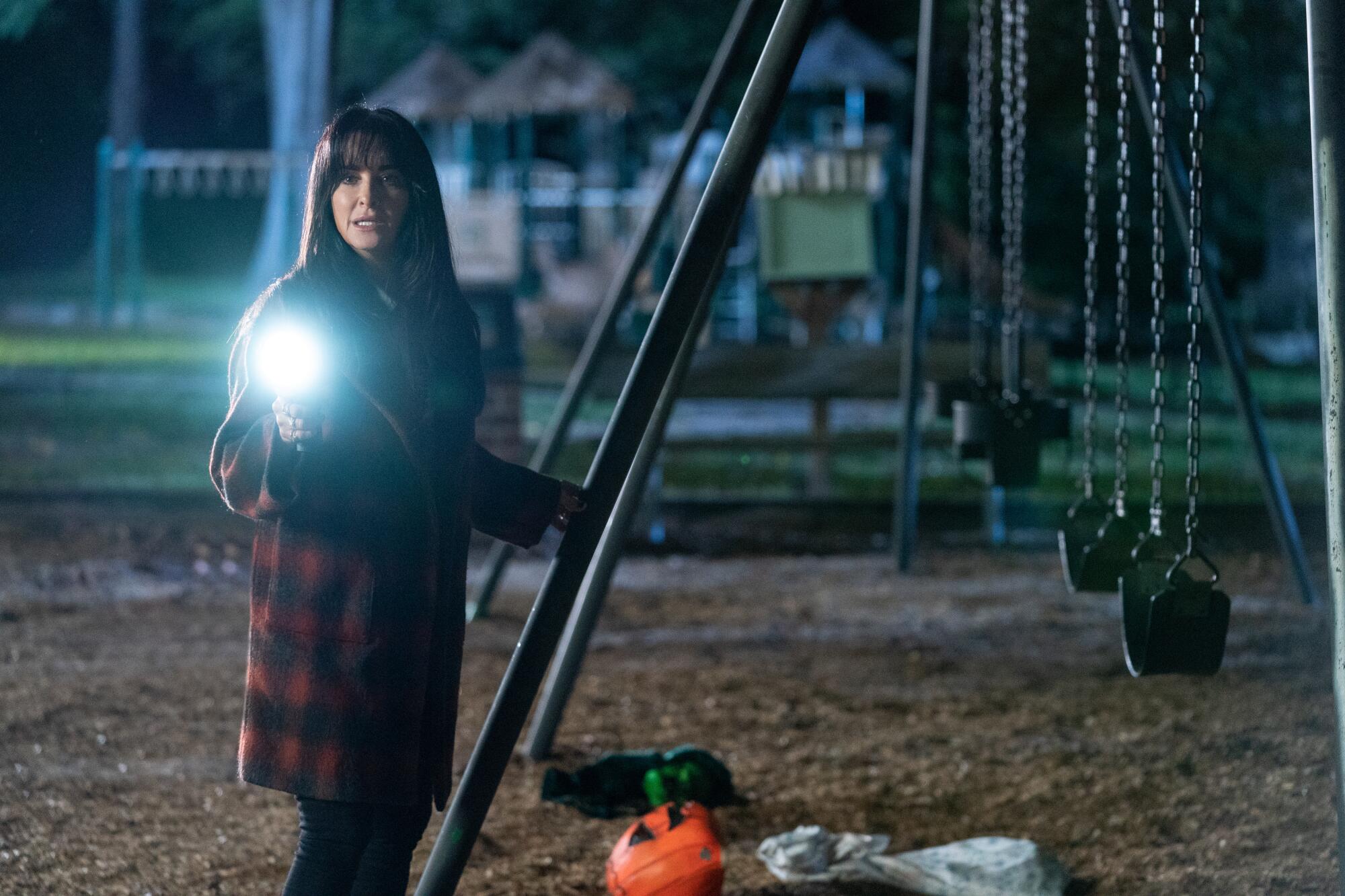 A woman holds a flashlight on a playground at night