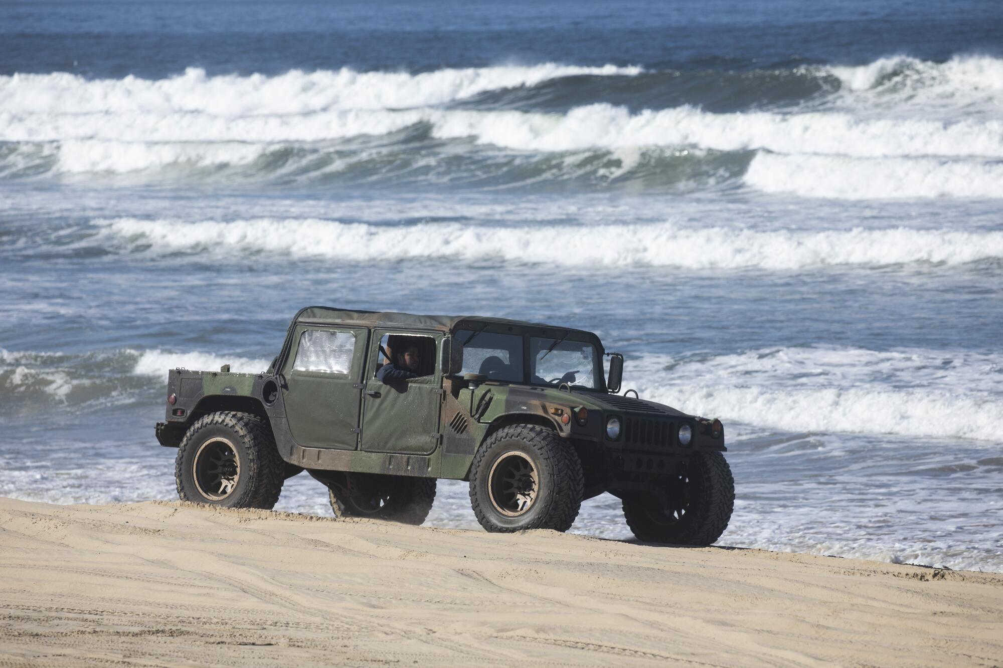 A military-style Humvee drives on on the beach near the water