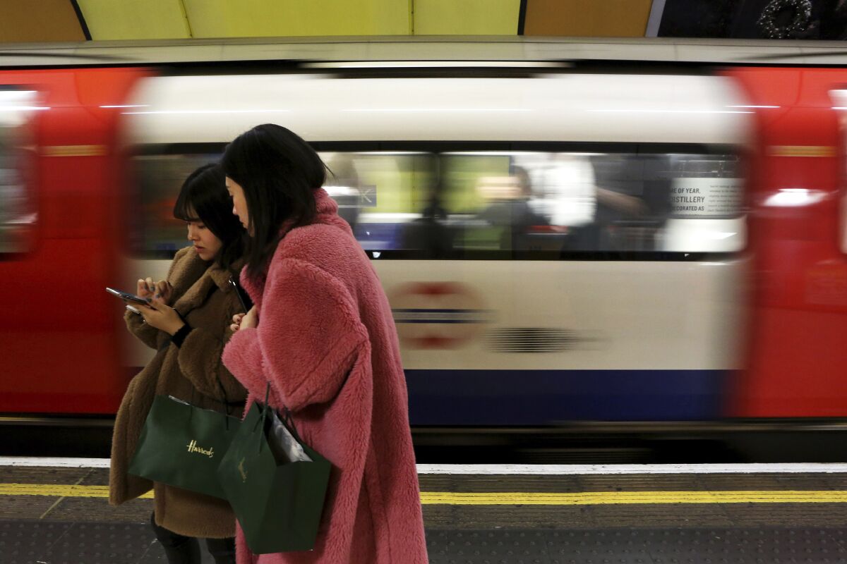 FILE - In this file photo dated Tuesday, Dec. 24, 2019, women use a cell phone on an underground platform in central London. Facebook's purchase of Giphy will hurt competition for animated images, U.K. regulators said Thursday Aug. 12, 2021, following an investigation, indicating the social network could be forced to sell off the company if the provisional finding's concerns are confirmed. Giphy's library of short looping videos, or GIFs, are a popular tool for internet users sending messages or posting on social media. (AP Photo/Petros Karadjias, FILE)