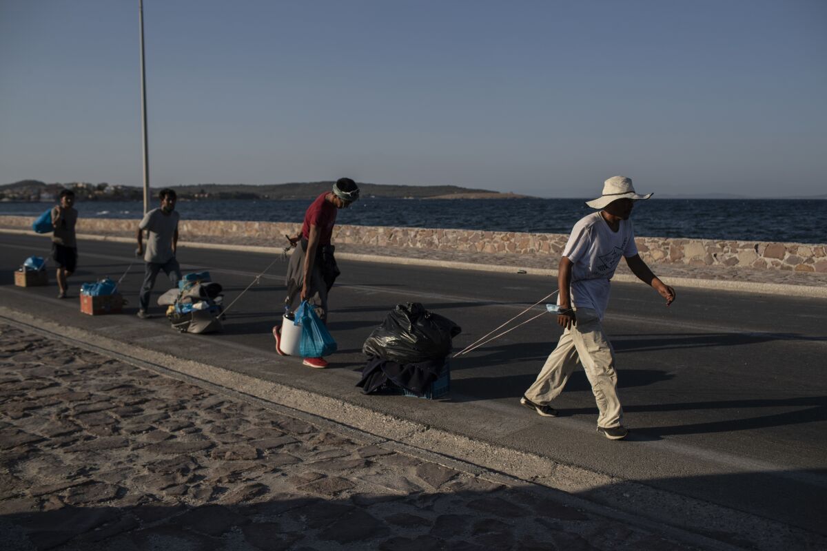 Migrants pull their belongings as they walk on a road near Mytilene town, on the northeastern island of Lesbos, Greece, Monday, Sept. 14, 2020. Greece's prime minister demanded Sunday that the European Union take a greater responsibility for managing migration into the bloc, as Greek authorities promised that 12,000 migrants and asylum-seekers left homeless after fire gutted an overcrowded camp would be moved shortly to a new tent city. (AP Photo/Petros Giannakouris)