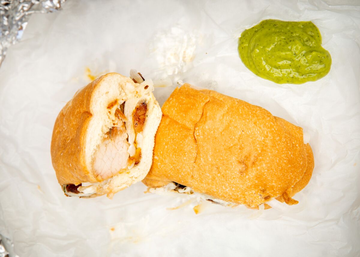 A fried pork sandwich, to-go, with green sauce made of cilantro, jalapenos, garlic, lime juice, avocado.