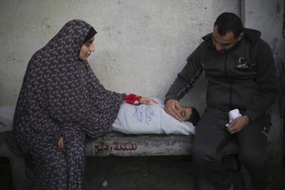 A man and woman sit next to the wrapped body of a child.