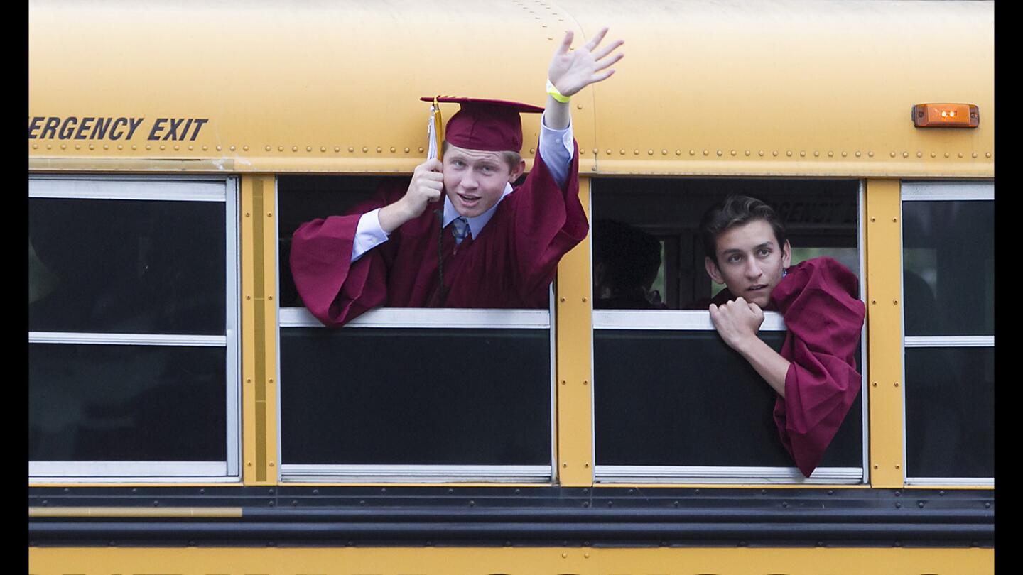 A graduate waves to family and friends from one of the buses arriving for the 2017 Laguna Beach High commencement ceremony at the Irvine Bowl on Thursday.