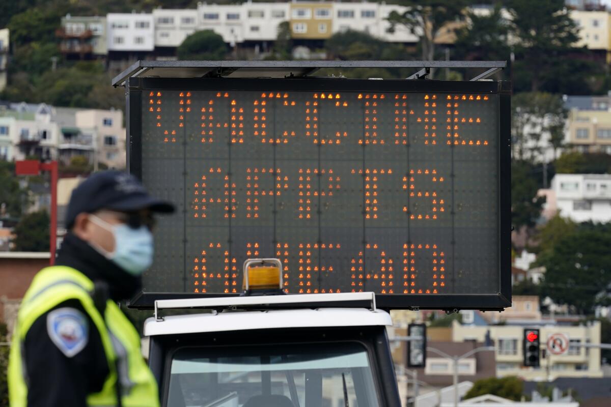 An officer stands in front of a sign about vaccine appointments at City College of San Francisco.