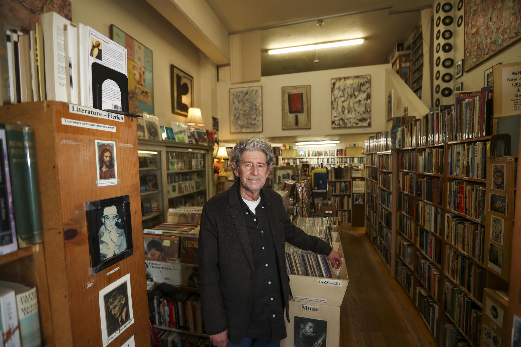 A man with curly gray hair standing in the middle of a bookstore.