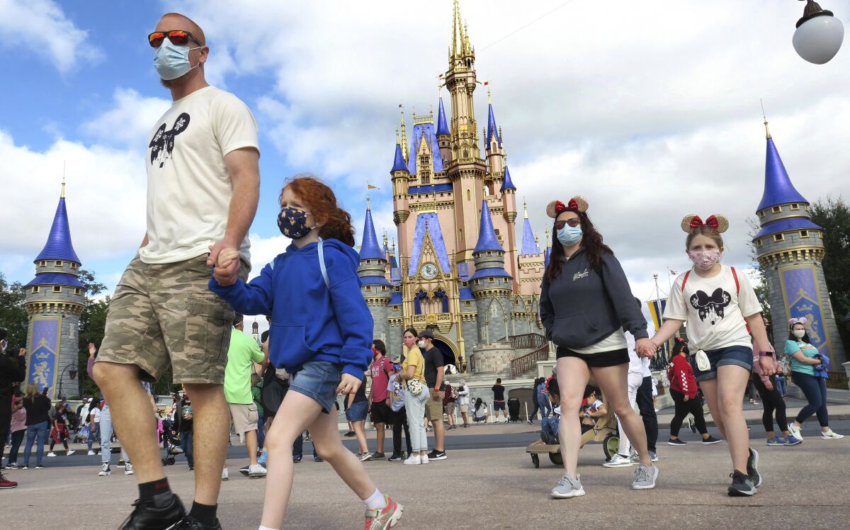 FILE - In this Monday, Dec. 21, 2020, file photo, a masked family walks past Cinderella Castle in the Magic Kingdom, at Walt Disney World in Lake Buena Vista, Fla. Walt Disney World is tweaking its face mask policy. Starting Thursday, Aug. 19, 2021, the theme park resort in Florida will allow visitors to chose whether or not to wear face coverings in outdoor lines, outdoor theatres and outdoor attractions. (Joe Burbank/Orlando Sentinel via AP, File)