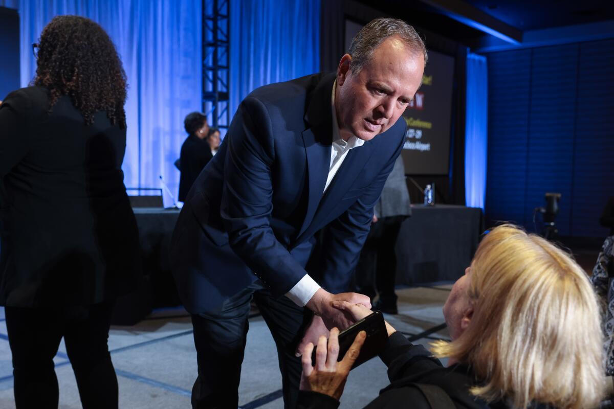Rep. Adam Schiff leans over from a stage to shake a woman's hand