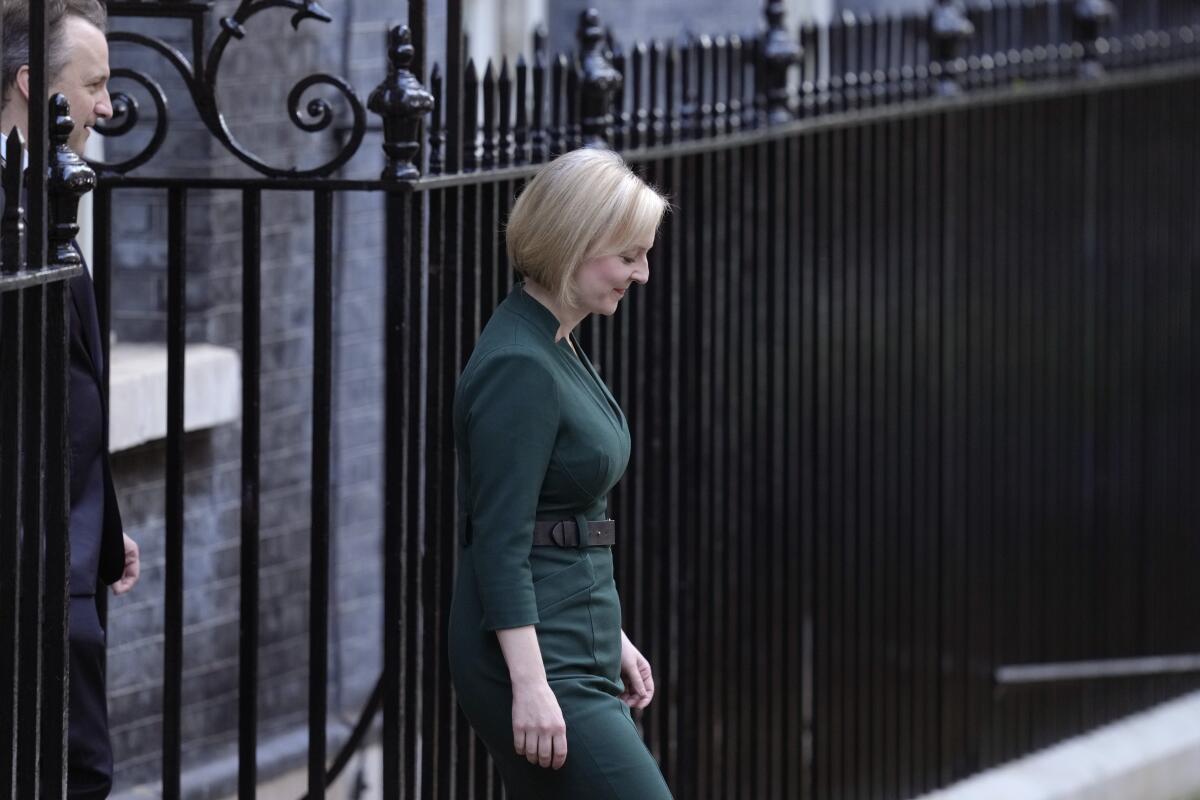 Liz Truss walks out of a gate with someone standing behind her 