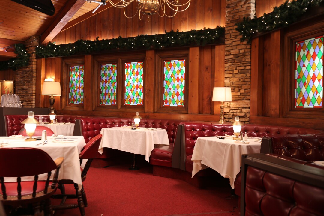 A restaurant interior with stained-glass windows and starched linens at red banquettes.