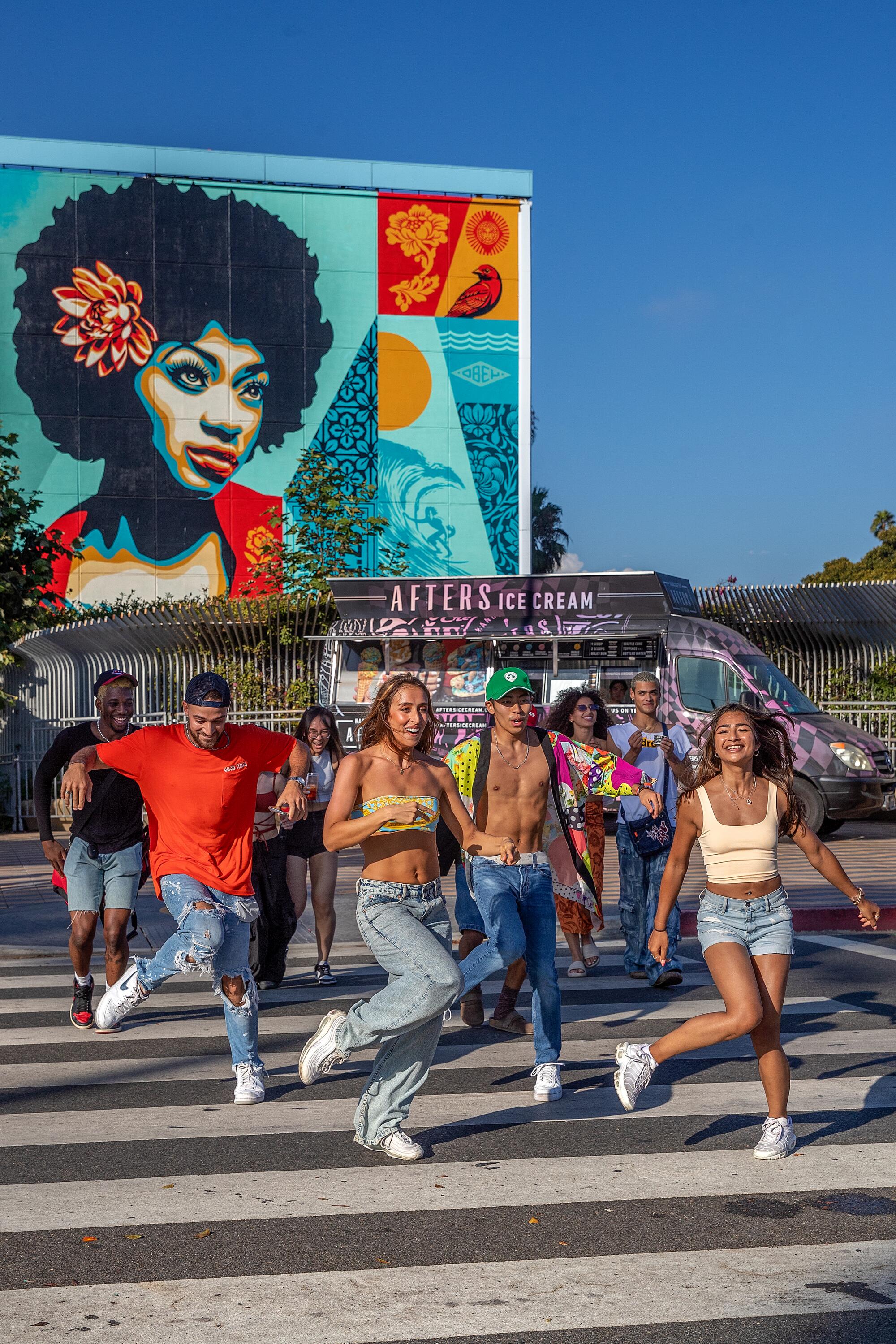 People dancing in a crosswalk in front of a colorful mural.