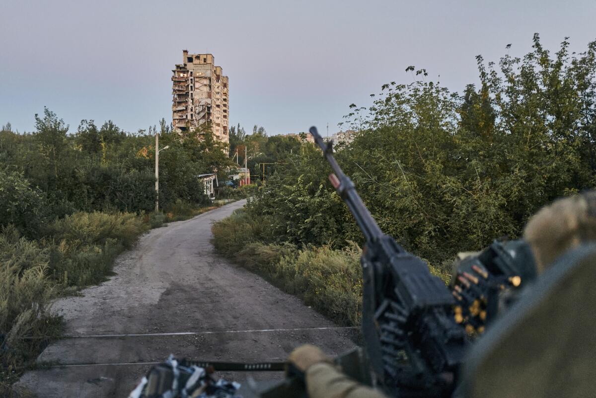 A Ukrainian soldier sits in his position on a road with a high-rise in the distance.