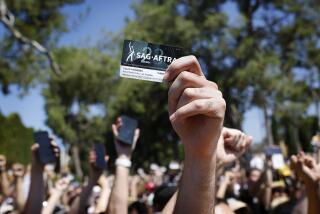 BURBANK-CA-AUGUST 22, 2023: SAG-AFTRA member Colin Borden holds up his membership card as SAG-AFTRA and WGA join forces with the AFL-CIO and its affiliates from across the nation and across industries for a national day of solidarity rally outside of Disney Studios in Burbank on August 22, 2023, fighting for fair contracts, better compensation, safe working conditions and protections from encroaching technology. (Christina House / Los Angeles Times)