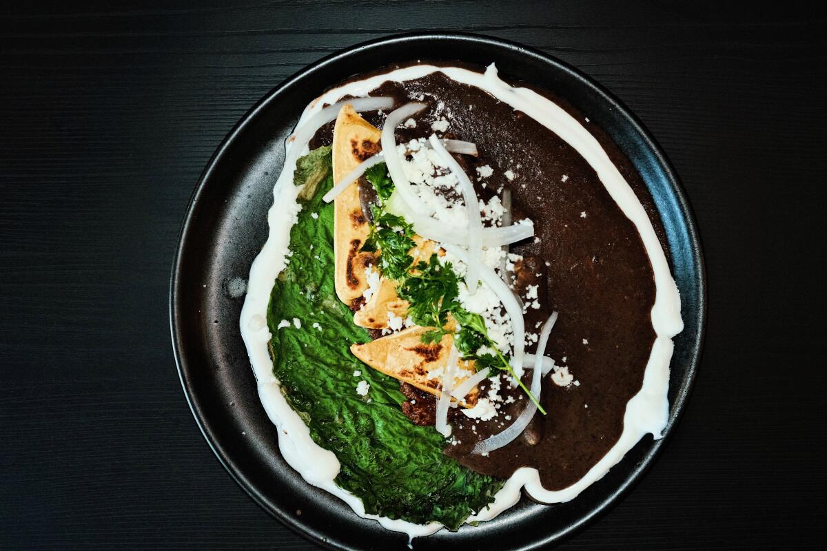 Tetelas on a black plate with refried black beans with quesillo-stuffed hoja santa 