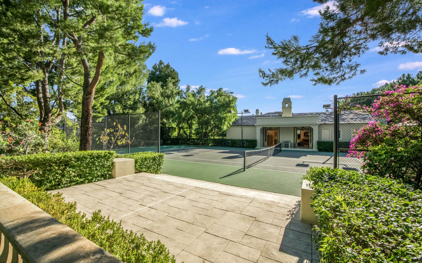 The tennis court is next to the home and greenery.