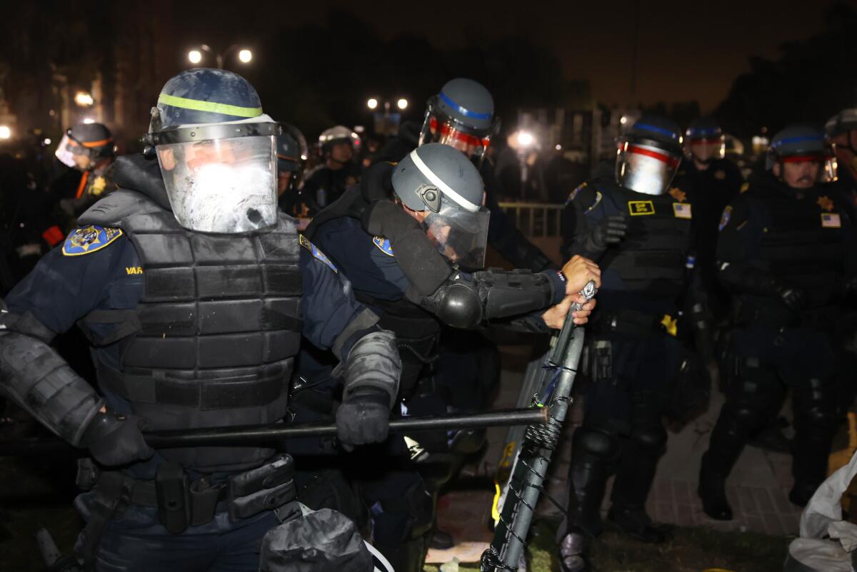 Police wearing helmets, masks and vests remove a barricade