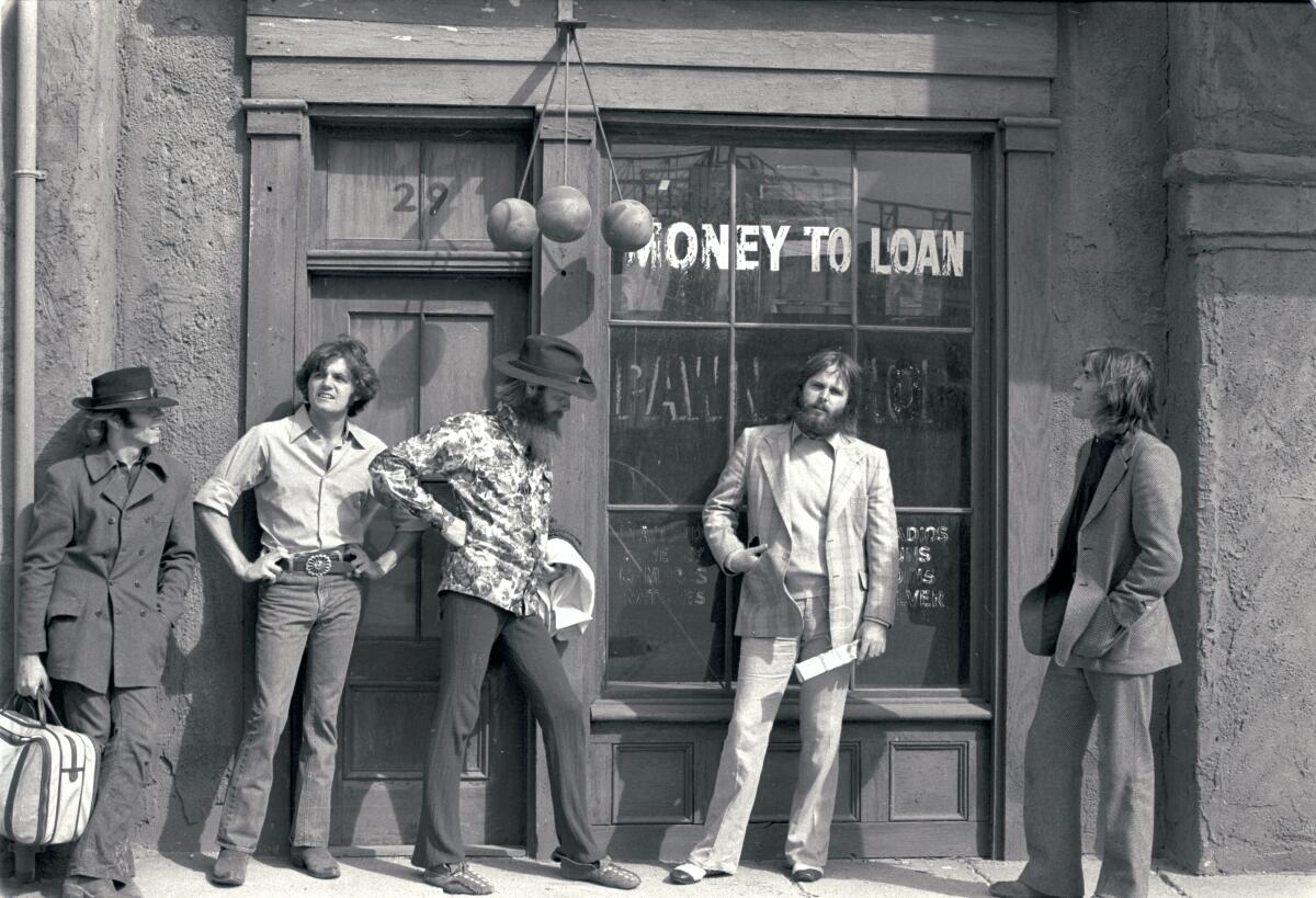 The Beach Boys stand outside a pawn shop, circa 1970, in a black-and-white photo.