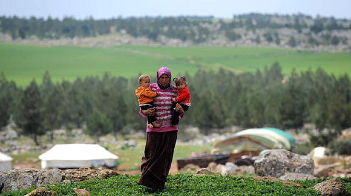 A Syrian woman carries her children near their makeshift refugee camp at the city of Afrin on the Syria-Turkey border.