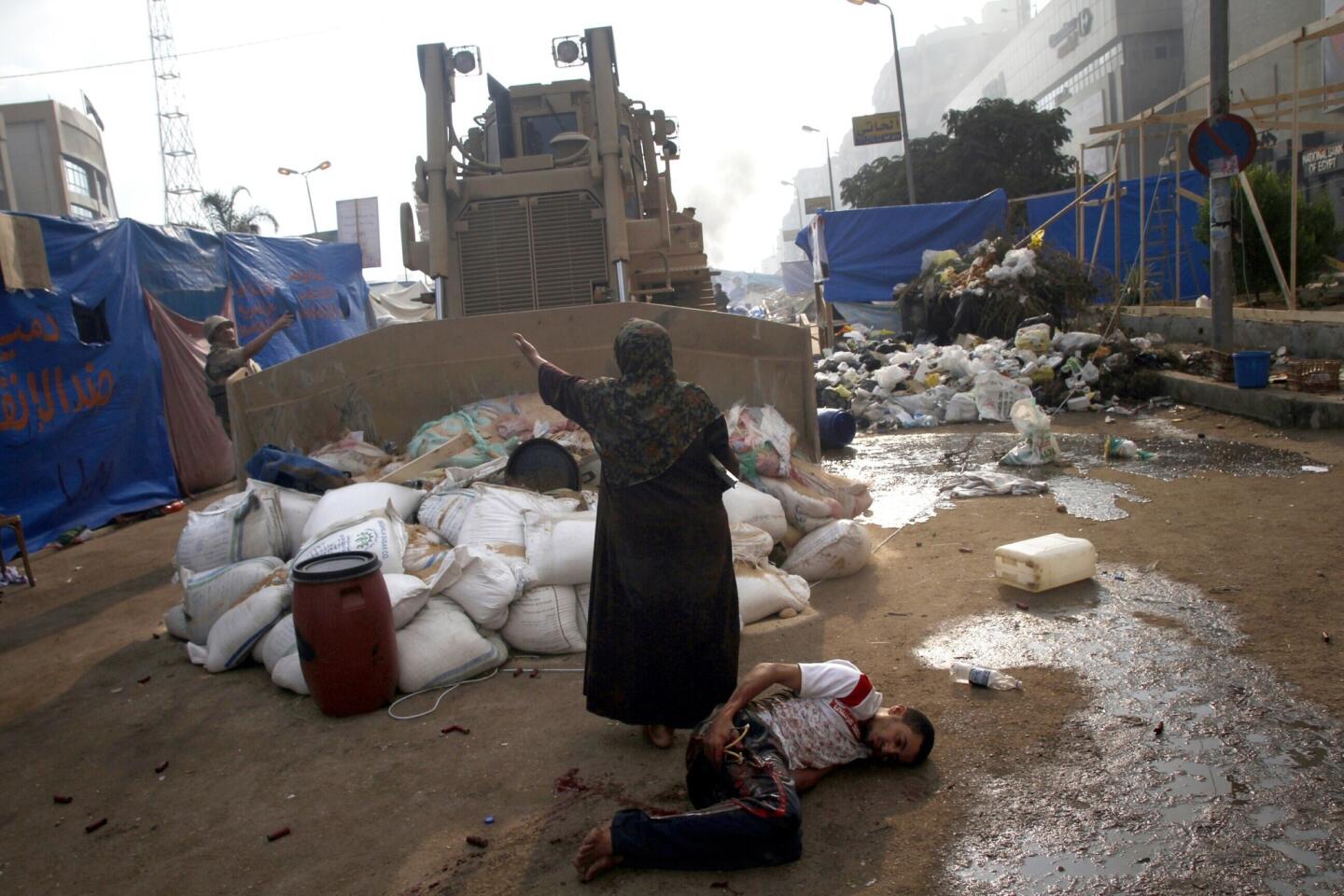 An Egyptian woman appeals to the driver of a military bulldozer as a wounded man lies in its path. Clashes between supporters of ousted President Mohamed Morsi and security forces spread across Egypt.
