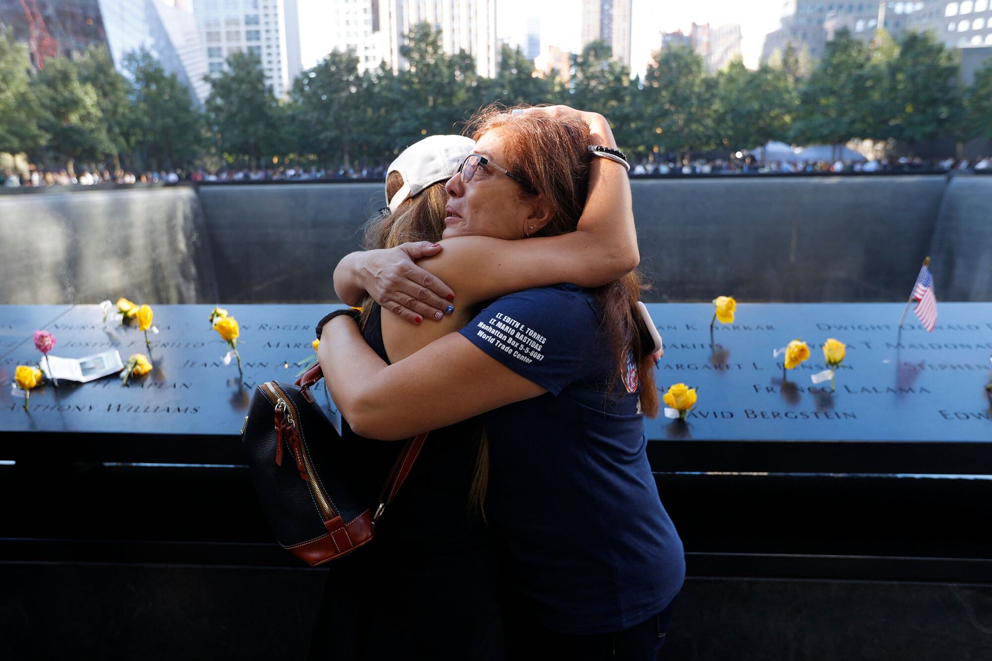 Two women embrace in front of a memorial.
