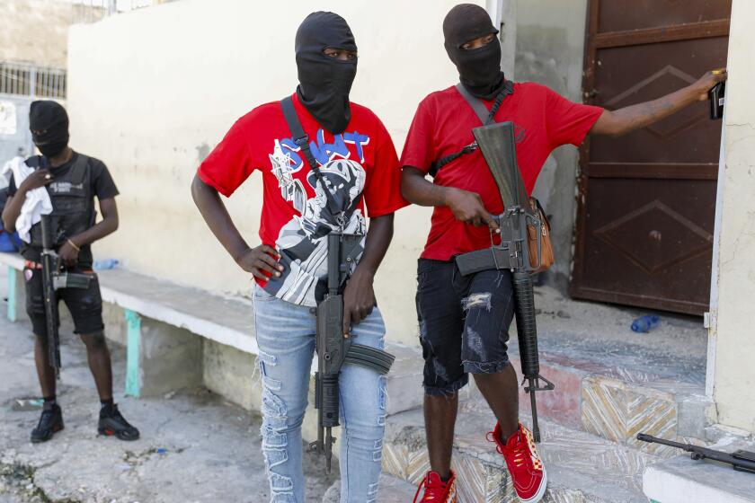 Masked members of "G9 and Family" gang stand guard during a press conference by their leader Barbecue in the Delmas 6 neighborhood of Port-au-Prince in Port-au-Prince, Haiti, Tuesday, March 5, 2024. Haiti's latest violence began with a direct challenge from Barbecue, a former elite police officer, who said he would target government ministers to prevent the prime minister's return and force his resignation. (AP Photo/Odelyn Joseph)