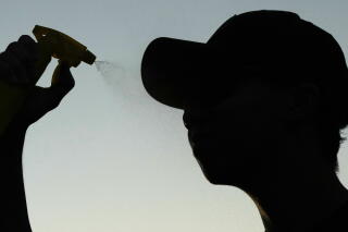 John Nguyen sprays water to cool off after shooting hoops during a hot weather day in Deerfield, Ill..